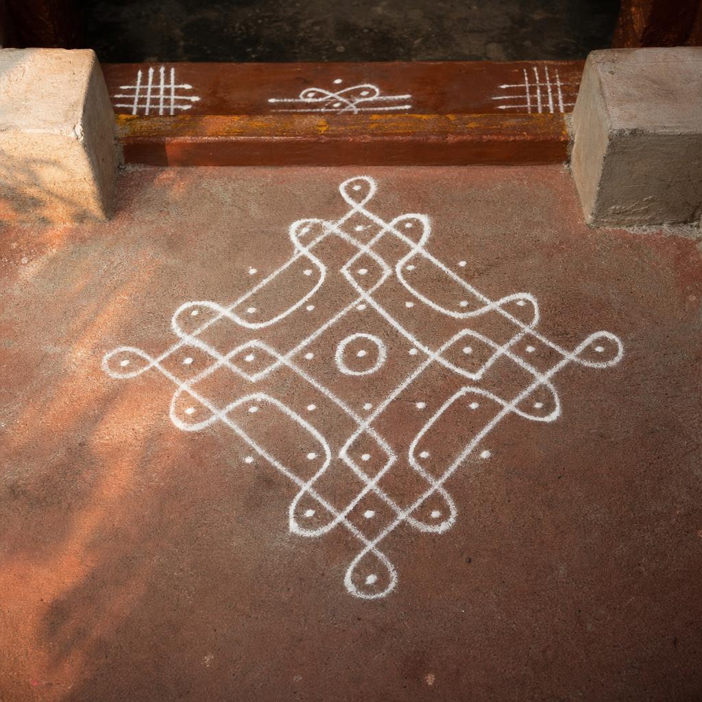 A hand-drawn white rice-flour muggu on a weathered terracotta doorstep at dawn